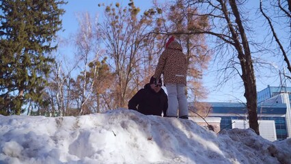 Wall Mural - Caucasian happy preschool girl plays with father with snow on a sunny winter day in a park