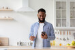© Prostock-studio - Happy young black man with glass of clear water in hand in minimalist kitchen interior, chatting on phone