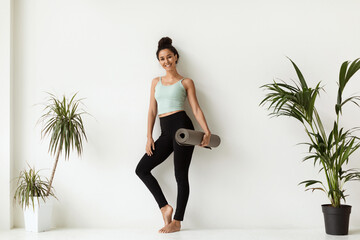 Wall Mural - Yoga Coach. Beautiful Smiling Woman Holding Fitness Mat Posing Near White Wall