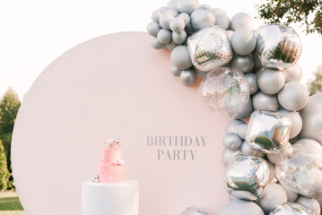 Wall Mural - A large pink cake with a pink photo zone of silver balloons on the background. Party decorated with balloons