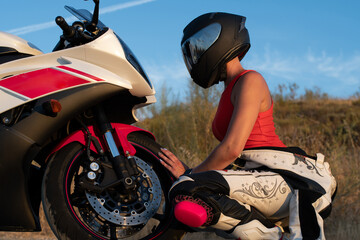 Wall Mural - young woman dressed as a biker with a safety helmet crouching down and leaning on the front wheel of her road motorcycle