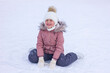 Cute little girl sitting on ice with skates after fall and laugh.