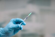 Close up of doctor's hand in medical gloves with a pulled up syringe ready for vaccination in front of a clinic room