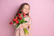 © Анна Брусницына - A little cute girl holding a bouquet of tulips Pink background. Happy women's day. Space for text. Bright Emotions.