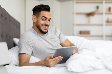 Wall Mural - Handsome Young Middle Eastern Guy Relaxing In Bed With Digital Tablet