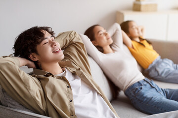 Calm happy young korean husband, wife and teen daughter relax on sofa with closed eyes in living room