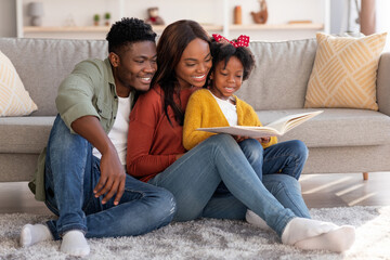 Wall Mural - Cheerful African American Family With Little Daughter Reading Book Together At Home