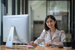 © Songsak C - Young beautiful Asian businesswoman working on her project with computer and smiling at the camera