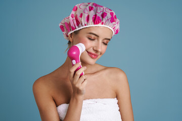 Wall Mural - Young woman wearing shower cap smiling while using facial massager