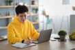 © Prostock-studio - Asian man sitting at desk, using pc writing in notebook
