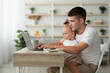 © Prostock-studio - Paternity Leave. Young Man Working On Laptop With Infant Baby On Laps