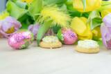 Wielkanocna, wiosenna aranżacja, tulipany, piórka, ciastka, kolorowe jajka, tło z miejscem na tekst.