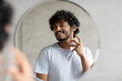 © Prostock-studio - Happy indian man looking in mirror spraying on cologne in bathroom interior, doing morning skincare routine