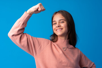 Little cute girl showing her strength on blue background