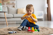 © Prostock-studio - Child development games. Engaged toddler boy playing with wooden colorful stacking and sorting toy, sitting on carpet