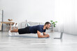 © Prostock-studio - Smiling young caucasian guy doing plank on mat on floor and look at laptop in living room interior, profile