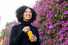 Smiling Black Woman With Juice Near Blooming Bush