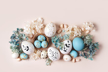 Easter Eggs With Sweets And Flowers On Beige. Happy Easter Concept. White And Blue Eggs And Cute Nest With Candy