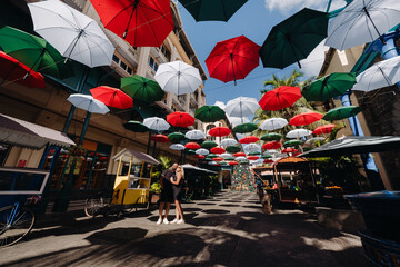 Port Louis, Mauritius, a black-clad couple stands on an umbrella-covered city alley leading to the capital