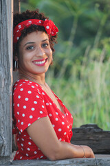 A young afro woman enjoys nature in a natural park. The girl is young and smiles at the camera. She is wearing youth clothing.