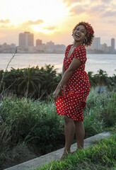 A young afro woman enjoys nature in a natural park. The girl is young and smiles at the camera. She is wearing youth clothing.