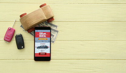 Wall Mural - Mobile phone with open car rent app, toy, keys and money on yellow wooden background