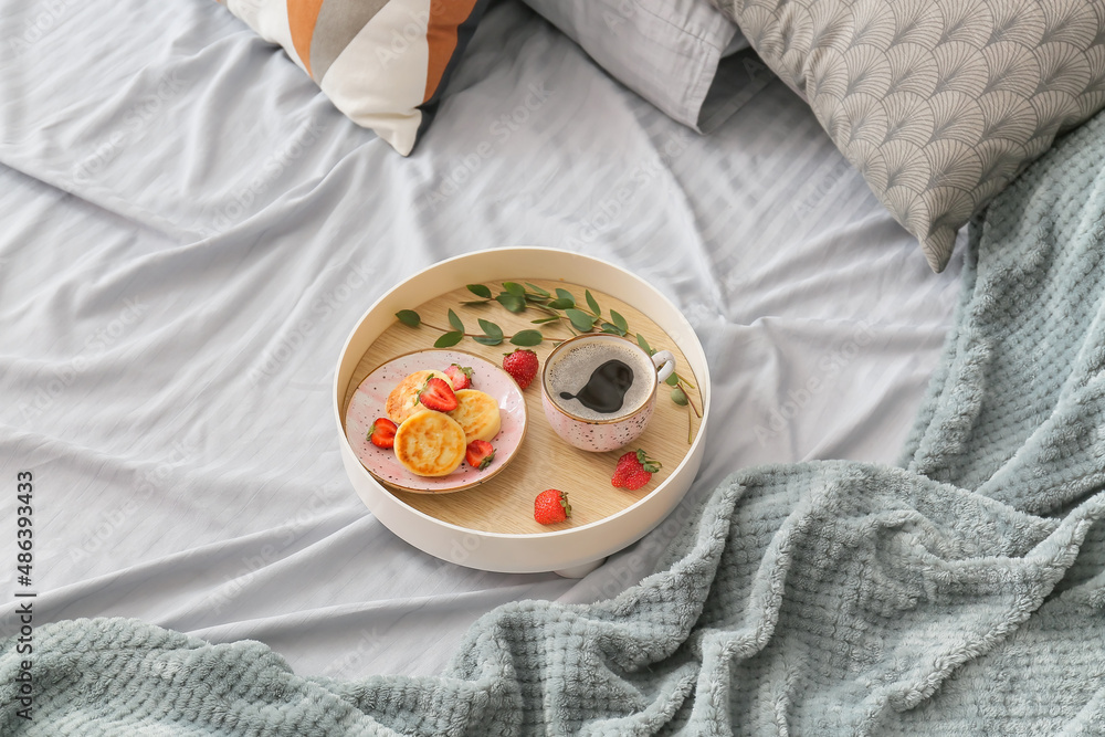Tray with tasty breakfast and eucalyptus branch on bed