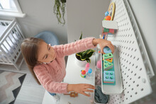 Cute Little Girl Taking Toys From Hanging Peg Board On Light Wall
