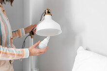 Woman Changing Light Bulb In Lamp Near Bed At Home