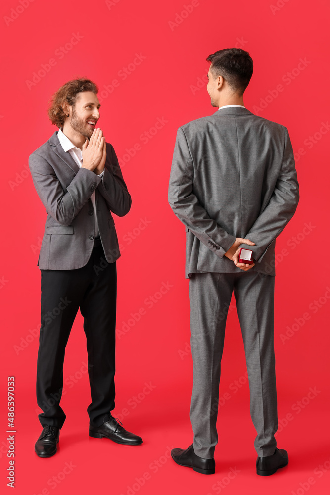 Young gay proposing to his boyfriend on red background