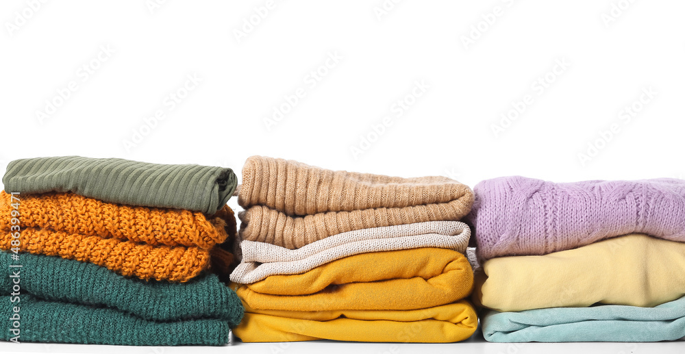 Stacks of stylish female sweaters on white background
