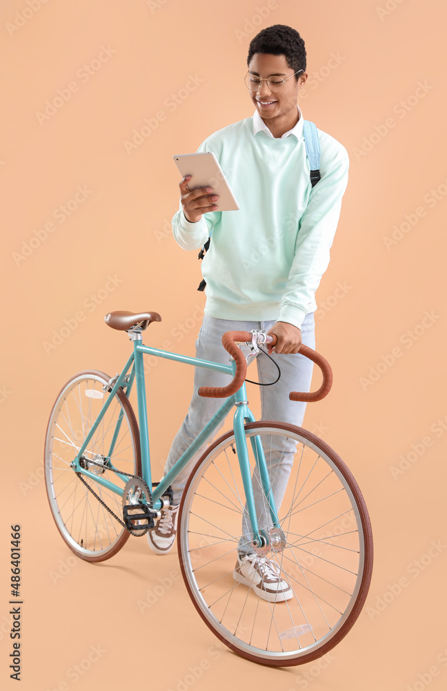 Male African-American student with bicycle and tablet computer on color background