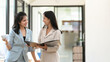 © bongkarn - Two businesswomen having a relax conversation in the office hallway.