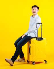 Portrait studio shot of millennial Asian young handsome male businessman traveler model in casual outfit sitting smiling on big trolley luggage traveling for business trip on yellow background