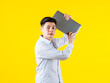 © Bangkok Click Studio - Portrait studio shot of millennial Asian young male businessman in casual outfit standing smiling holding laptop computer on yellow background
