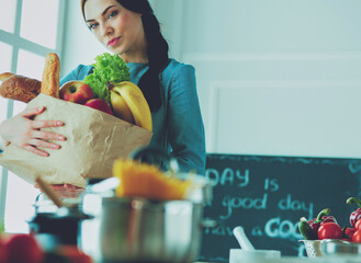 Young woman holding grocery shopping bag with vegetables .Standing in the kitchen