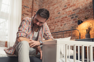 novice dad sitting next to the cradle feeling terrified about his infant baby's future . High quality photo