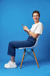 © fotofabrika - Cheerful attractive young woman holding smartphone, enjoying chatting or online shopping against blue background