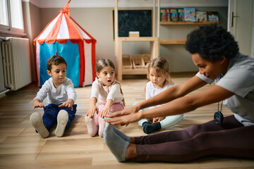 Group of kids and their teacher stretching during exercise class at preschool.