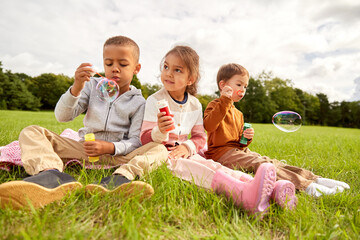 childhood, leisure and people concept - group of children blowing soap bubbles at park