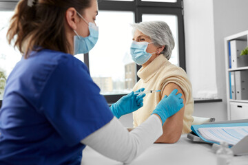 Sticker - medicine, health and vaccination concept - doctor or nurse with syringe making vaccine or drug injection to senior woman in mask at hospital