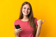 © luismolinero - Young woman using mobile phone isolated on yellow background pointing to the side to present a product