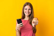 © luismolinero - Young woman using mobile phone isolated on yellow background points finger at you with a confident expression