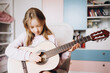 © Анна Молько - a cute little girl in a pink sweater is playing a baby guitar in her room. music training