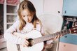 © Анна Молько - a cute little girl in a pink sweater is playing a baby guitar in her room. music training