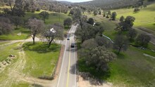 Drone Aerial Following A Truck Though A Winding Road In A Oak Forest.
