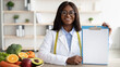 African american doctor nutritionist holding blank clipboard, showing mockup for right nutrition menu, copy space