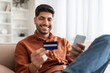 © Prostock-studio - Smiling Arab guy using phone and credit card at home