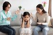 Unhappy Asian girl covering ears while angry mother and grandmother scolding her at home. Family problems concept