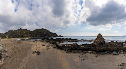 Sticker - panorama view of a secluded sandy beach on a wild mountainous coastline with rocks